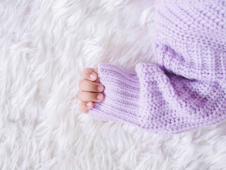 Close up of newborn baby hand is wearing a purple clothes on white bed