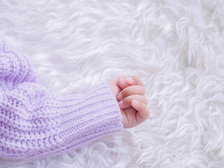 Close up of newborn baby hand is wearing a purple clothes on white bed