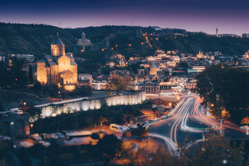 Tbilisi old town glowing at night with light trails from moving cars © EdNurg