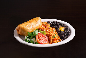 Burrito platter with rice, black beans and a fresh garden side salad in a white dish on a dark surface; copy space