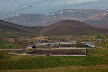 Kabardino-Balkaria, Russia-10.05.2025: Rural landscape featuring green fields, farm buildings, and distant mountains under a cloudy sky.