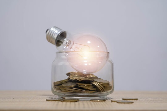 Glass jar filled with coins and a glowing light bulb symbolizing financial ideas, investment planning, energy savings, innovation, and economic growth in a clean minimalist business concept.