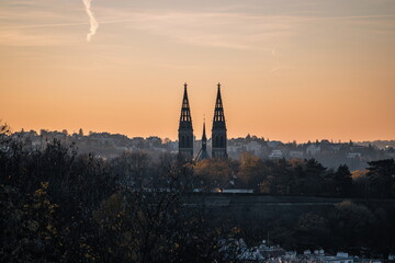 Naklejka premium Twin Gothic towers rising over Vyšehrad, silhouetted against a glowing Prague sunset sky.