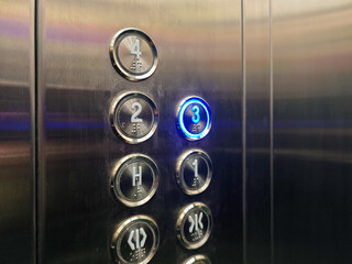 Close-up of an elevator control panel featuring an illuminated button for the third floor, showcasing accessibility with braille and modern design elements; ideal for transportation themes.
