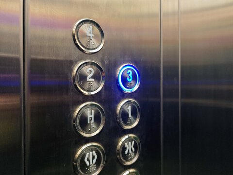 Close-up of an elevator control panel featuring an illuminated button for the third floor, showcasing accessibility with braille and modern design elements; ideal for transportation themes.
