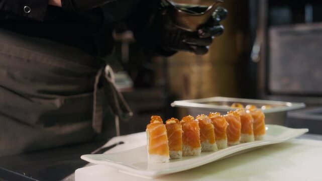 Cinematic close up shot of unrecognizable male chef putting caviar on salmon sushi roll with gloved hands while preparing for serving in professional restaurant kitchen, copy space