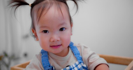 Cute Asian toddler smiling and looking at camera, wearing a blue checkered apron, creating a joyful and playful atmosphere.