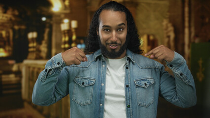 Man points finger to chest in church building, denim jacket and white shirt visible; faith identity confidence.