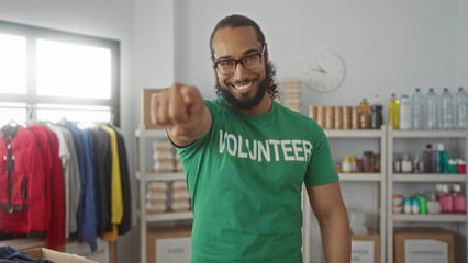 Man pointing finger toward camera in donation building wearing green volunteer shirt and smiling; community encouragement.