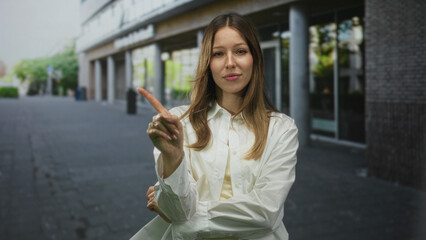 Woman pointing index finger at camera on street, crossed arms and white shirt visible; confidence boundary assertion resolve.