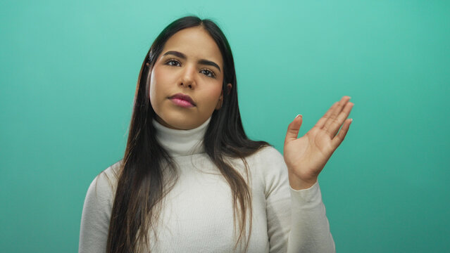Young woman with long hair wearing turtleneck waves against green background, emanating friendly and approachable vibe, ideal for communication concepts.