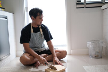 A man in a black apron sits on the floor with a book in front of him