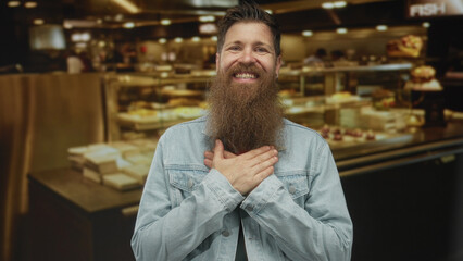 Fototapeta premium Young man with beard smiling broadly places hand on chest in busy indoor restaurant; gratitude sincerity.