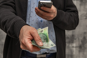 A man in a blue shirt and sweater holds money in his hand, counting the money