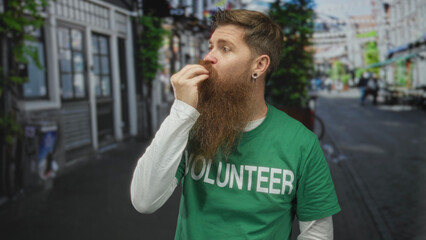 Young bearded man blowing kiss on busy city street wearing green volunteer shirt; affection generosity kindness compassion.