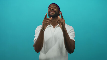 Man pointing fingers at camera in studio with teal backdrop, wearing white polo and smiling...