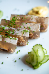 Close-up of aspic slices garnished with chopped herbs on a white plate with cucumber garnish.