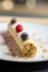 Rolled pastry filled with nuts and topped with fresh blueberries and raspberries on a white plate