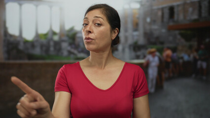 Hispanic middle age woman with arms crossed and pursed lips in front of roman ruins building; determined confidence.