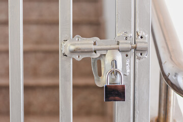 A silver padlock secures a metal gate with stairs behind.