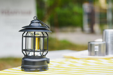 A black camping lantern sits on a yellow and white table.