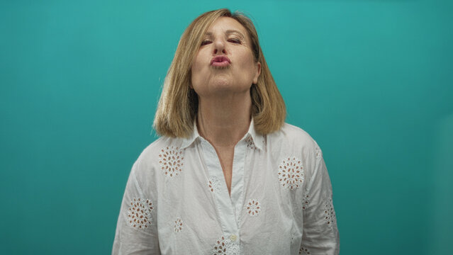 Woman makes heart gesture with hands after pursing lips in a studio setting; affection connection.