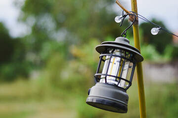 A camping lantern hangs from a bamboo pole outdoors.