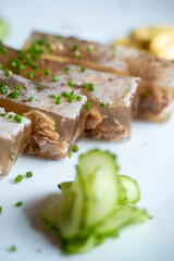 Close-up view of a gourmet aspic dish garnished with fresh chives and served with sliced cucumber on a white plate.