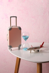 Toy luggage and airplane, Hourglass on table, pink concrete background. Travel time