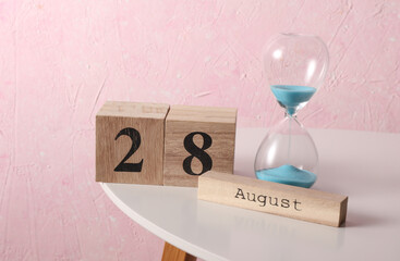August 28 wooden block calendar and hourglass on table, pink concrete background