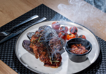 Grilled steak topped with herbs alongside roasted cherry tomatoes and a smoky sauce on a ceramic plate