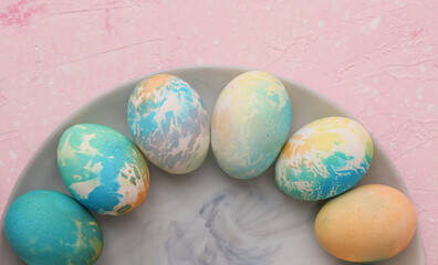 Colored Easter egg in plate on pink pastel background. Top view