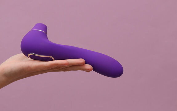 Female hand holding sex toy vacuum vibrator on purple background