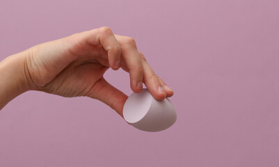 Makeup egg blender sponge in woman hand on purple background. Beauty concept