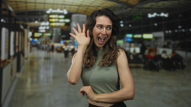 Young hispanic woman with pouting lips standing in airport terminal amid blurred departure gates; playful. - Powered by Adobe