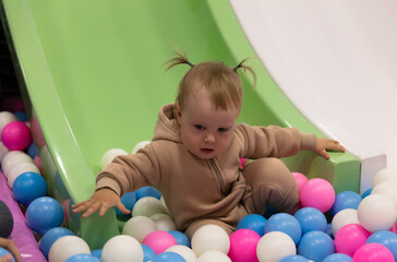 Little baby slides down a slide into a dry pool with balls at a children's entertainment center