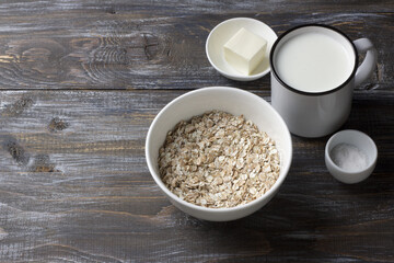 Four grain flakes with milk, butter and salt in white bowl on rustic wooden table for healthy breakfast preparation