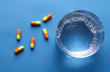 Pills and glass of water on blue background