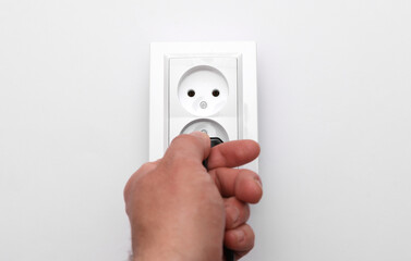 Hand inserting an electric plug into an electrical outlet on a white background