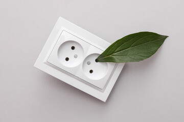 Green energy. Electrical outlet with green leaf on grey background