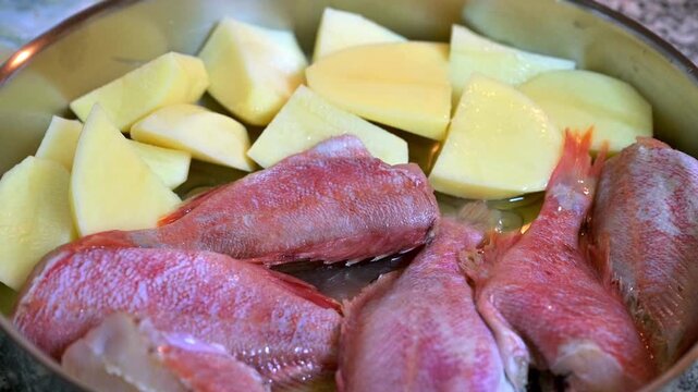 The raw redfish (red mullet) and potatoes in a baking pan