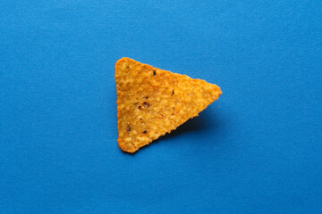 Triangular appetizing corn tortilla chip slice on blue background