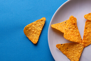 Triangular appetizing corn tortilla chips slices  in plate on blue background