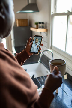 Adult focused on telehealth call with mature doctor in kitchen