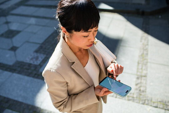 Young adult woman focused on smartphone on urban sidewalk