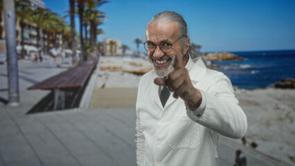 Scientist man in lab coat with long gray hair points finger at camera on seaside street promenade;...