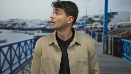 Man raises eyes then rolls them on pier while a carefree male traveler of hispanic heritage enjoys...