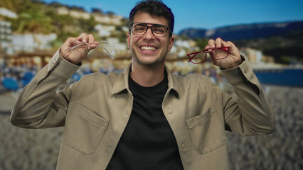 Man displays glasses while holding them up at beach scene featuring hispanic host smiling beside specs frames and showcasing eyewear on vacation.