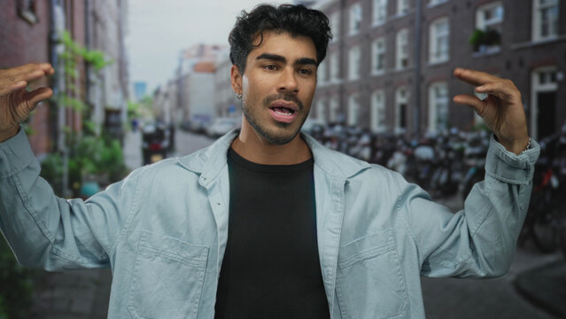 Man gesturing with hands on bustling urban street flanked by brick buildings and parked bicycles; enthusiastic communication.