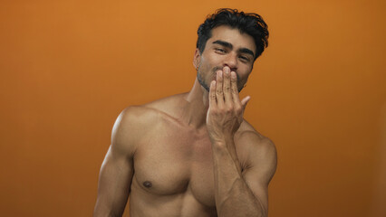 Fototapeta premium Man blowing a kiss with parted lips and muscular chest in an orange studio setting showing his relaxed head tilt and smile; affection romance.
